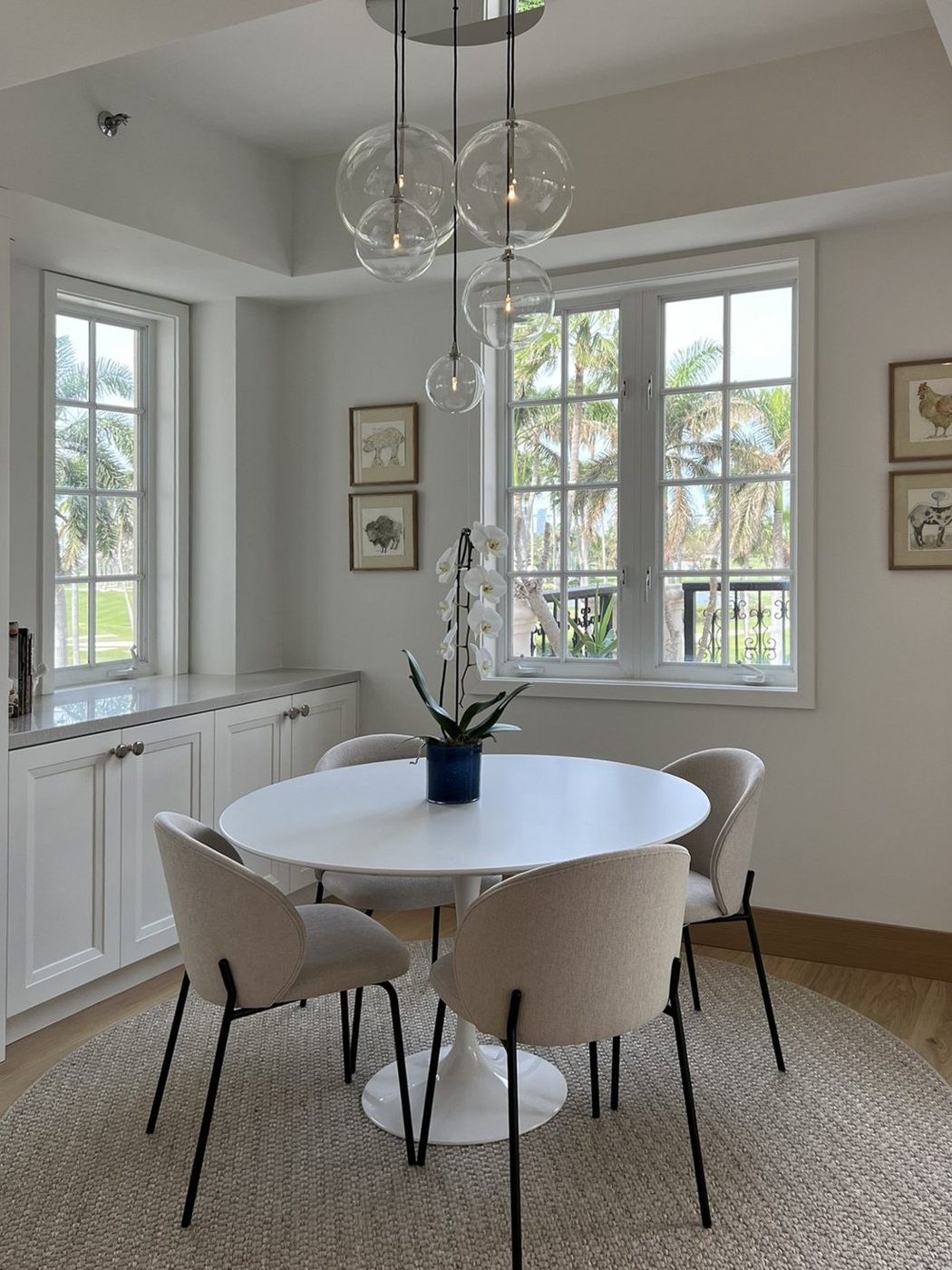 Breakfast room with a round white pedestal table, upholstered chairs, glass globe pendant and palm views