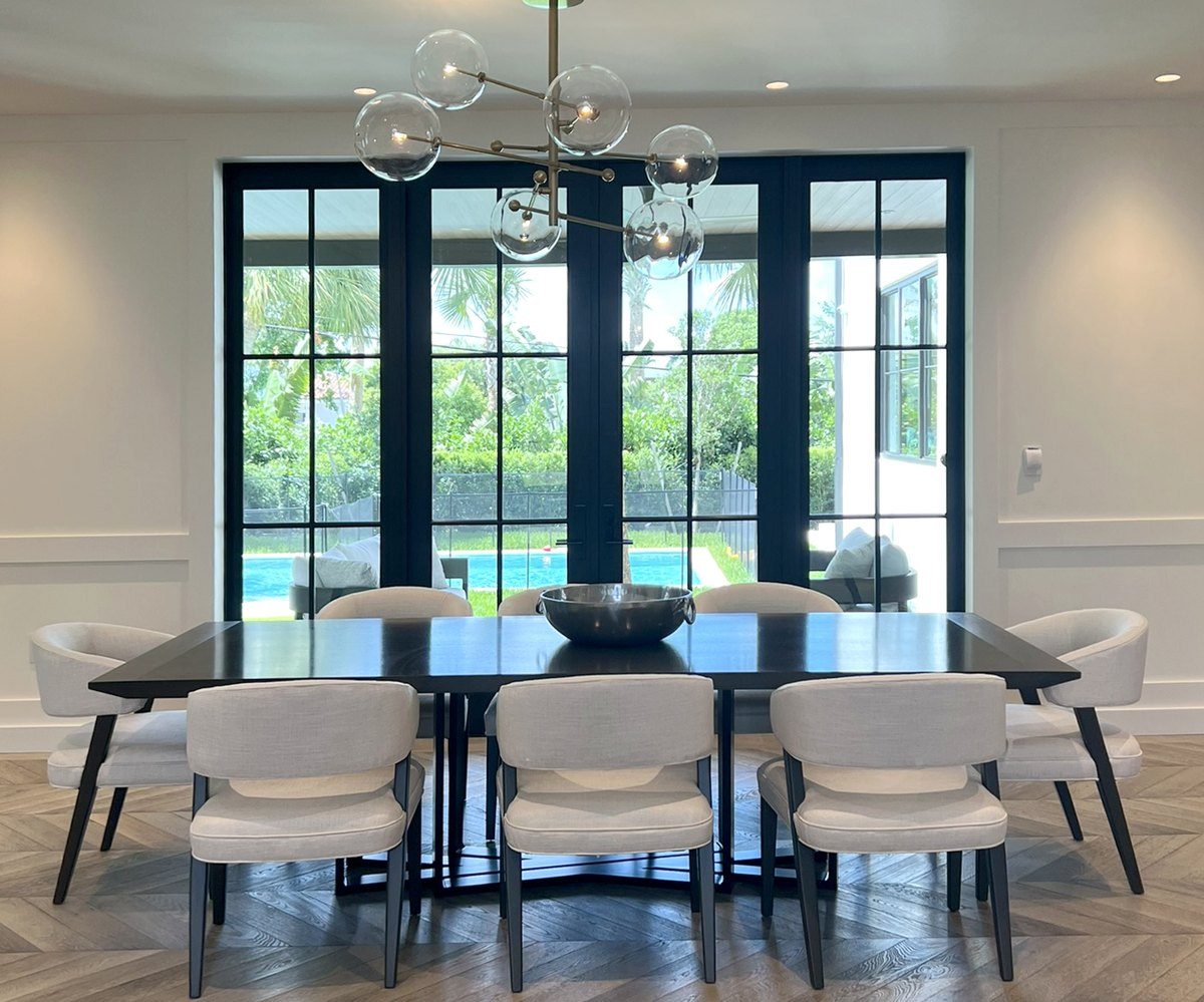 Dining room with a dark wood table, linen chairs and a glass globe chandelier facing steel-framed doors to the pool