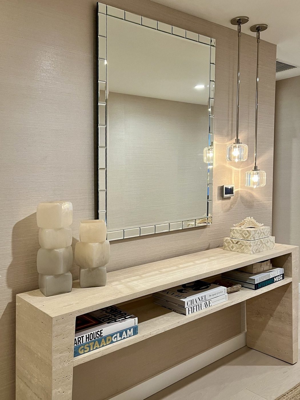 Entry with a travertine waterfall console, alabaster vases, beveled mirror, glass pendants and styled books