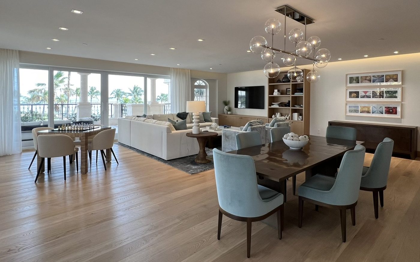 Open great room with a white sectional, game table and dining area overlooking palms and water