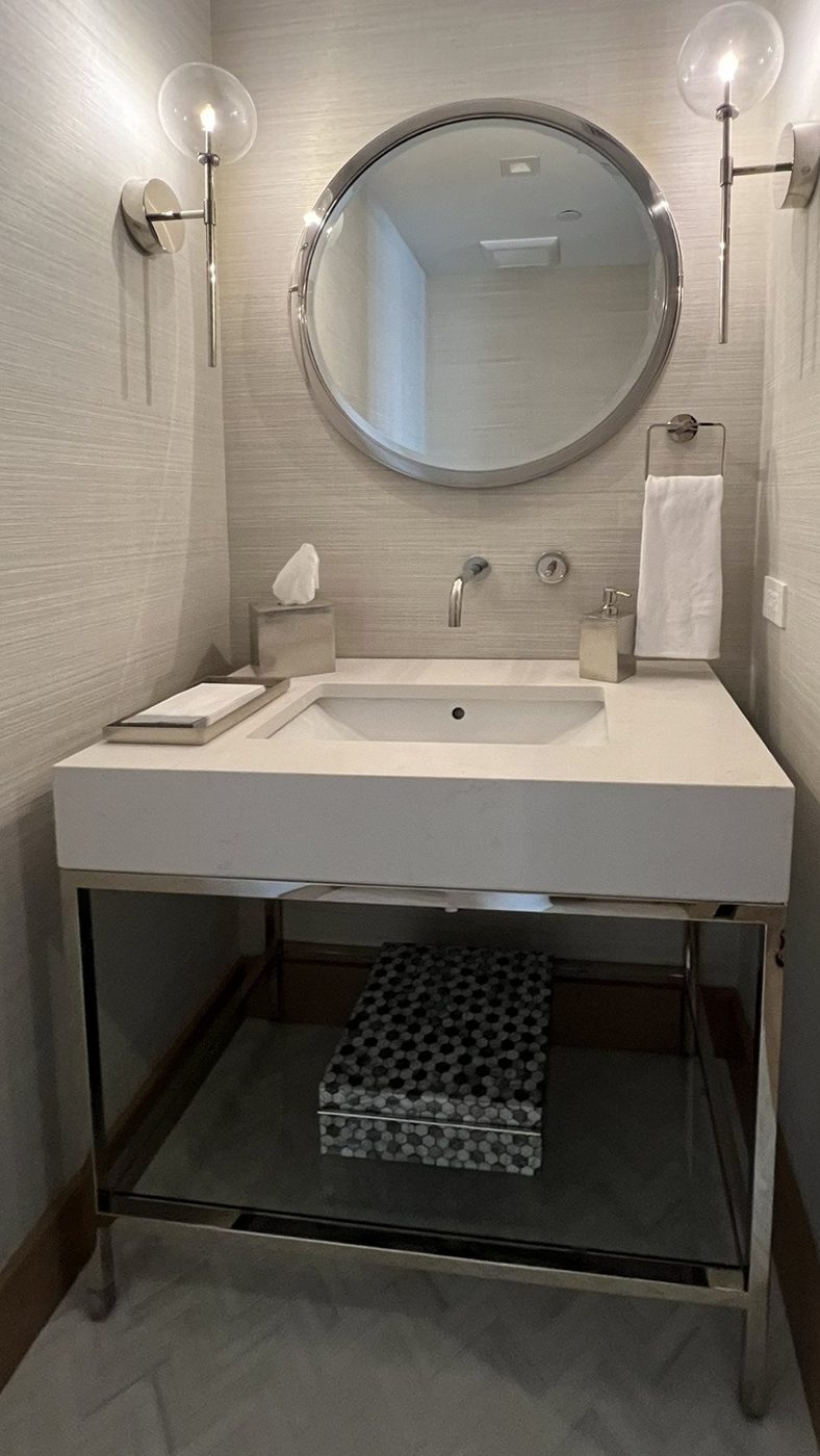 Powder room with grasscloth walls, a round polished-nickel mirror, glass globe sconces and a floating stone vanity