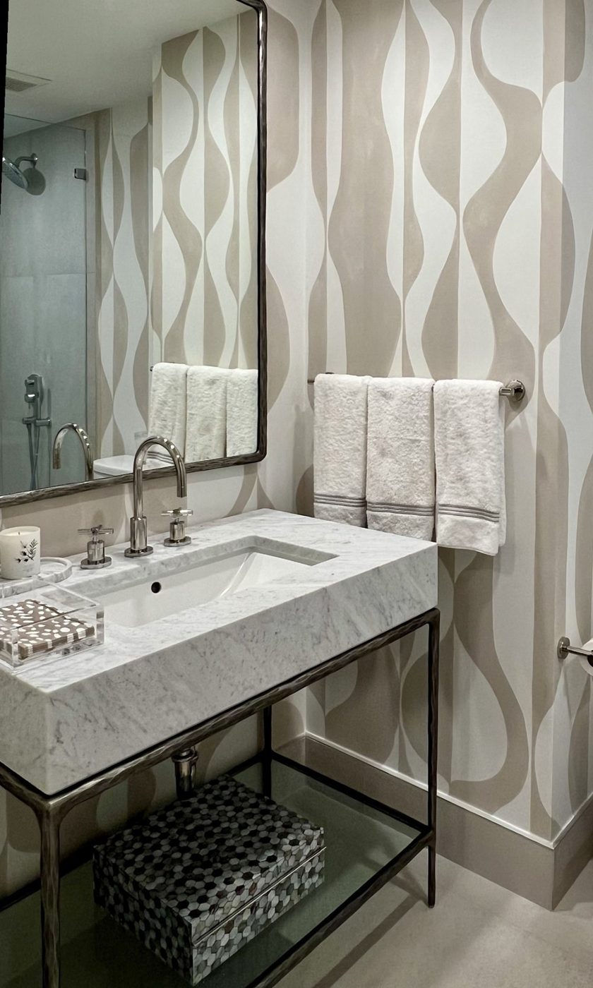 Powder room with hand-painted wave wallpaper, a marble vanity on a bronze stand, mother-of-pearl box and white hand towels